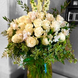 Cream roses and white flowers in a glass vase with greenery