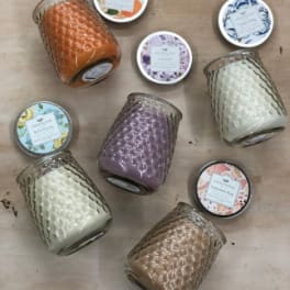 Assorted colored jar candles with patterned lids arranged on a light wood surface