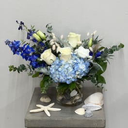 Blue and white floral arrangement in a glass vase with seashells and a starfish