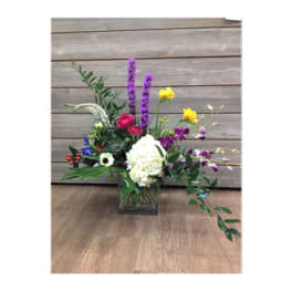 Mixed floral arrangement in a square glass vase with purple, white, yellow, and pink blooms
