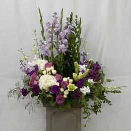 Tall floral arrangement with purple, white, and pink blooms in a pedestal container