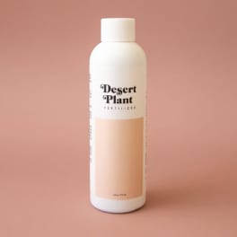 White bottle labeled Desert Plant Fertilizer on a pink background