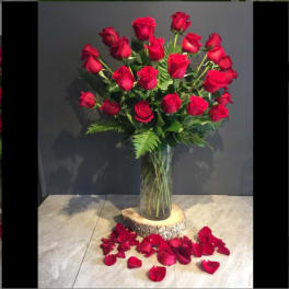 Tall bouquet of red roses in a clear glass vase with rose petals below