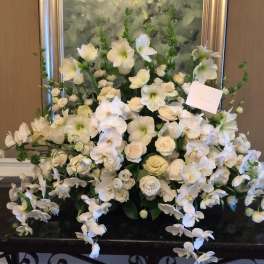 Large white floral arrangement with orchids and roses in a black container
