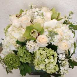 White and pale green floral arrangement with roses and orchids in a vase