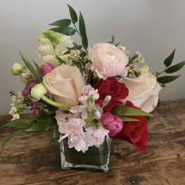 Mixed bouquet of roses, ranunculus, and snapdragons in a square glass vase