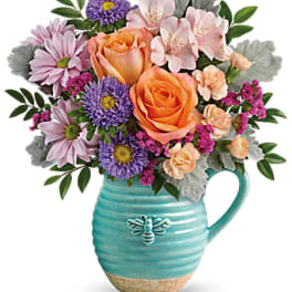 Bouquet of peach roses, pink daisies, and purple flowers in a turquoise pitcher vase