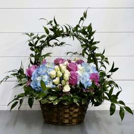 Basket arrangement of blue hydrangeas and purple roses with greenery arch