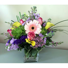 Mixed bouquet with pink gerbera daisies, roses, and purple flowers in a glass vase