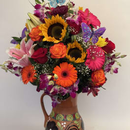 Colorful bouquet of sunflowers, roses, lilies, and gerbera daisies in a painted vase