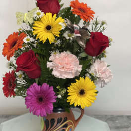 Mixed bouquet of roses, gerbera daisies, and carnations in a decorative mug