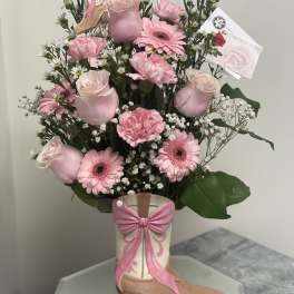 Pink flower arrangement in a decorative boot vase with a bow