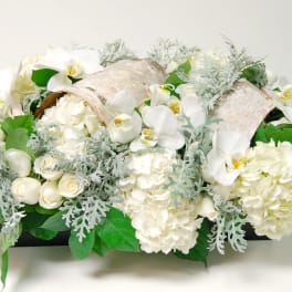 White floral arrangement with orchids and hydrangeas in a low container