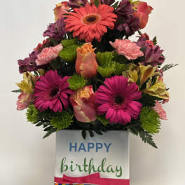 Birthday flower arrangement in a striped gift box with a "Happy Birthday" topper