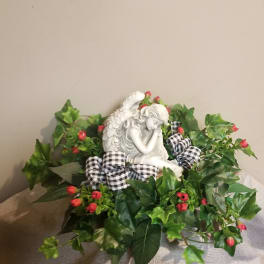Angel figurine surrounded by red berry-like flowers and ivy with a plaid ribbon