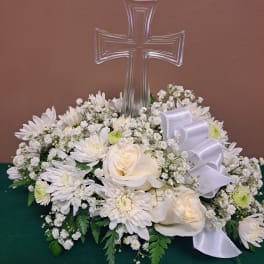 White floral arrangement with a clear cross centerpiece and white ribbon