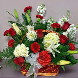 Basket arrangement of red roses, carnations, lilies, and white blooms with a ribbon bow