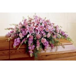 Pink and lavender floral casket spray on a wooden casket