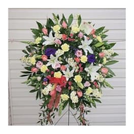 Standing floral spray with lilies, roses, and carnations in pink, white, yellow, and purple