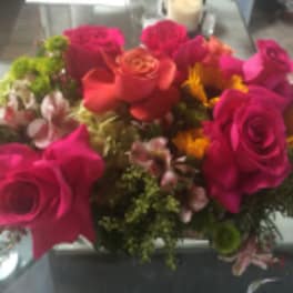 Compact arrangement of hot pink and orange roses with yellow blooms in a glass vase