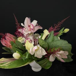 Pink and white flowers arranged in a white vase with broad green leaves