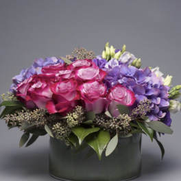 Pink roses and purple hydrangeas arranged in a dark round box