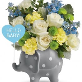 Bouquet of white, yellow, and blue flowers in a gray elephant vase with a baby sign
