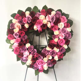Heart-shaped wreath of pink, lavender, white, and red roses on a stand