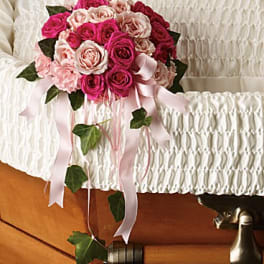 Pink and blush rose bouquet with trailing ribbon on a white casket
