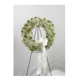 White floral wreath on a black stand with a white ribbon bow