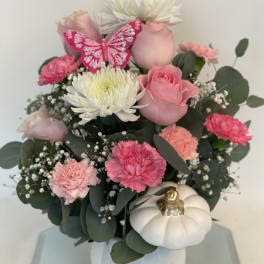 Pink and white flower arrangement in a white pumpkin vase with a butterfly decoration