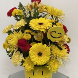 Yellow and red mixed bouquet in a smiley-face vase with emoji accents
