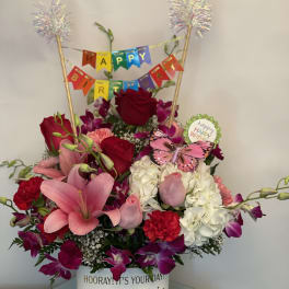 Birthday flower arrangement with roses, lilies, and hydrangeas in a decorated container