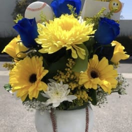Yellow and blue flower arrangement with a baseball and smiley card in a white vase