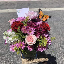 Bouquet of pink and red flowers in a glass vase with a butterfly pick