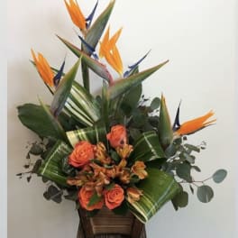 Tropical arrangement with orange birds of paradise and coral roses in a wooden container