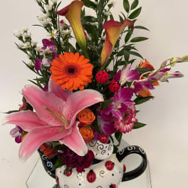 Colorful mixed bouquet with lilies, gerbera daisies, orchids, and roses in a ladybug teapot