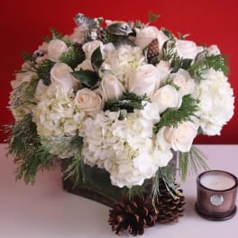 White roses and hydrangeas in a dark vase with pinecones and a candle