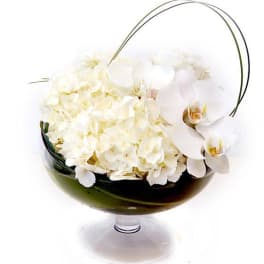 Low arrangement of white hydrangeas and orchids in a clear glass pedestal bowl