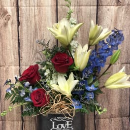 Red roses and pale lilies in a black container with a "Love" sign