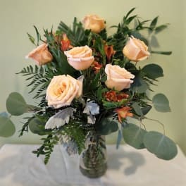 Peach roses in a glass vase with mixed greenery