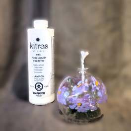 Purple floral candle in a glass dome beside a bottle of lamp oil