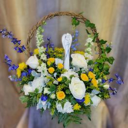 Basket of white and yellow flowers with blue accents and a small angel figurine