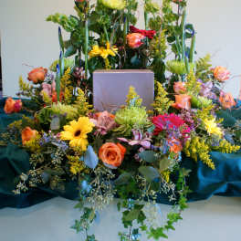 Large floral arrangement with roses, daisies, and tall greenery around a box
