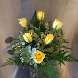 Yellow roses arranged in a glass vase with mixed greenery