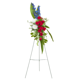 Standing floral spray with red roses, white blooms, and blue flowers on an easel