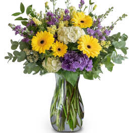 Bouquet of yellow gerbera daisies and purple flowers in a glass vase