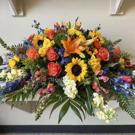 Large colorful floral casket spray with roses, sunflowers, lilies, and orchids