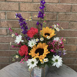 Mixed bouquet with sunflowers, daisies, carnations, and purple spikes in a tin container