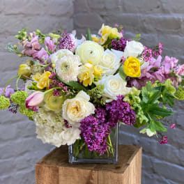 Mixed bouquet in a square glass vase with white, pink, yellow, and purple flowers